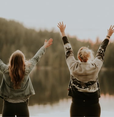 Two happy people with arms raised, standing by a lake, celebrating the positive impact of care from Archway Mental Health.