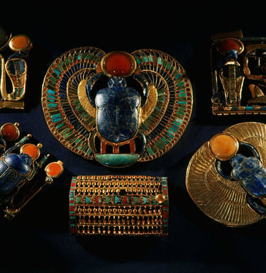 Ancient Egyptian gold jewelry featuring lapis lazuli scarab beetles and carnelian stones.