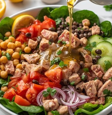 Healthy tuna salad bowl with chickpeas, tomatoes, and olive oil dressing being poured.