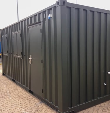 Dark green modified shipping container office with a steel door and side windows on a paved area.