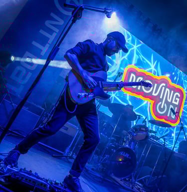 Foto real del guitarrista de Moving On tocando en un evento y el logo proyectado en pantalla