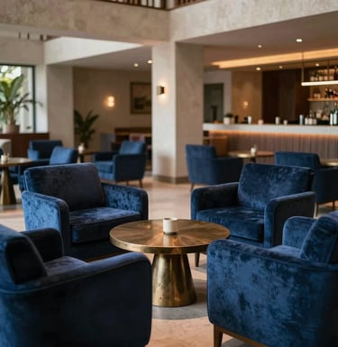 A wide shot of an empty, luxurious private lounge area in Brazil. Deep blue velvet armchairs arranged around a low bronze table. Architecture is modern with South American influences. Soft, warm indirect lighting creating a peaceful mood.