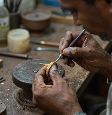 A documentary-style photograph of master artisans in a traditional Kolkata workshop, carefully handcrafting an 18K gold-plated bracelet with precise tools and artistic dedication.
