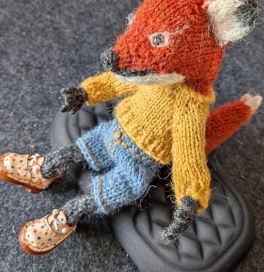 a small knitted fox sitting on top of a black shoe