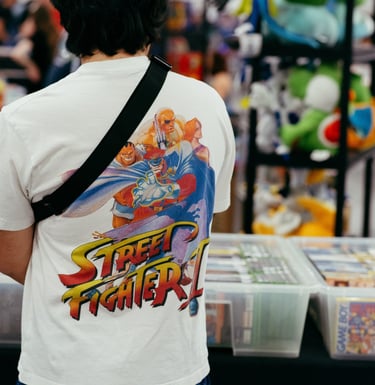A man wearing a street fighter video game shirt looks at games for sale