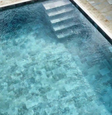 Overhead view of a modern backyard swimming pool with blue mosaic tile and stone patio.