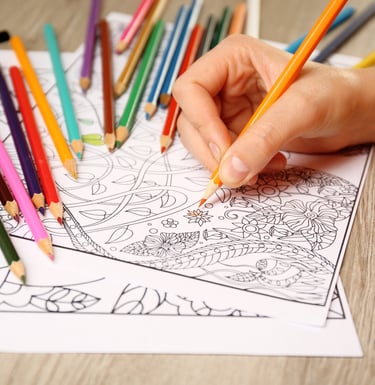A person coloring an intricate floral adult coloring book page with vibrant colored pencils.