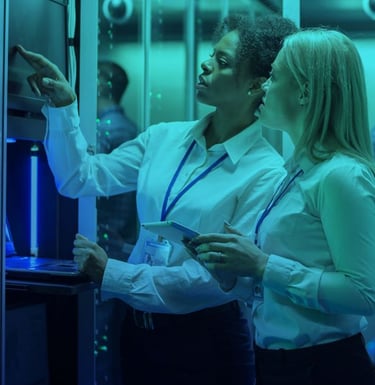 two women in a server room with a laptop