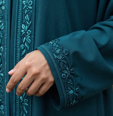 A detailed close-up shot of a hand-embroidered abaya sleeve in dark teal fabric. The focus is on the intricate threadwork and the rich texture of the textile. Middle Eastern aesthetic.