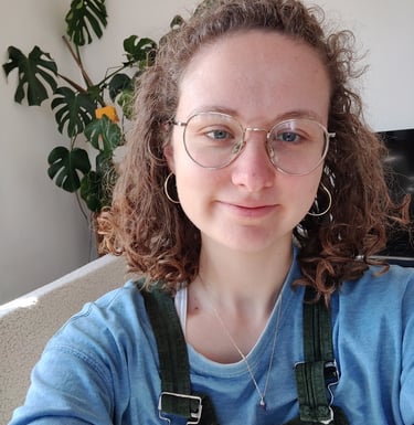 a selfie of Eleanor who is a curly haired queer women in her late twenties wtih glasses and dungarees