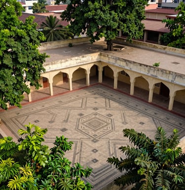 A high-angle shot of a traditional South Asian Pakistani school courtyard with geometric tile patterns and lush green trees, daytime photography.