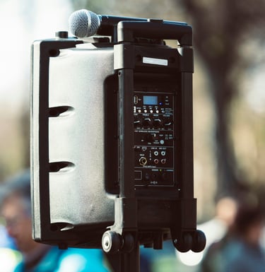 Portable PA system speaker with a microphone mounted on top for outdoor public speaking events.