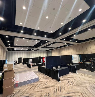 Empty convention hall setup with black drapes, exhibitor booths, and modern ceiling lighting.