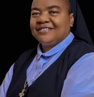 Smiling Catholic nun wearing a blue habit and silver cross necklace against a black background.