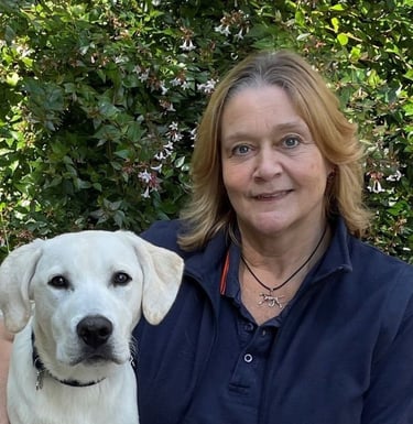 A woman is sitting with her arm around a young yellow labrador