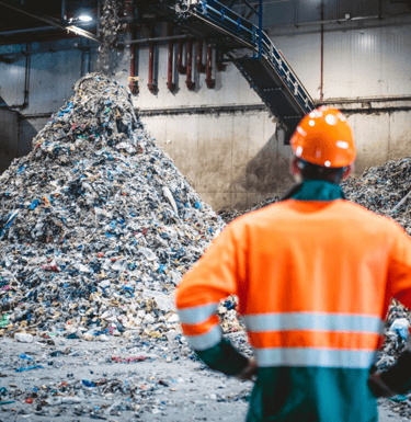 a man in a safety vest standing in front of a pile of garbage