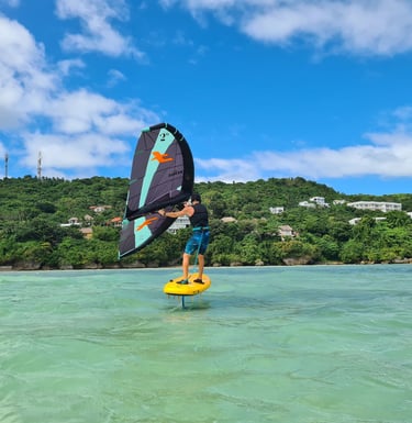 a man holding a wing on a beginner foil board in the middle of crystal clear water in a lagoon