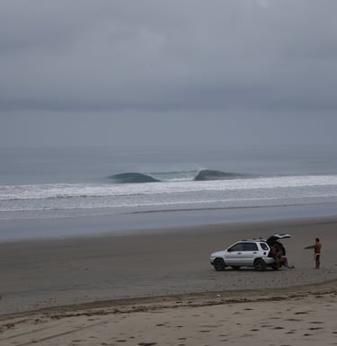 A perfect unridden wave with surfers watching from the beach
