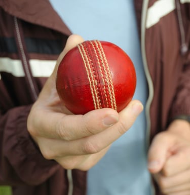 man's hand holding a red cricket hard ball