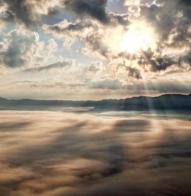 Fog-covered mountains with sunbeams piercing through dramatic clouds.