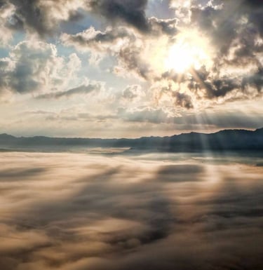 a view of a mountain range with clouds and sun shining through the clouds