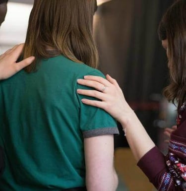 Three people placing hands on someone’s back and shoulders in a moment of comfort.
