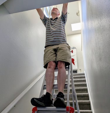 Cyd hanging a framed photo on a stairwell using an adjustable ladder