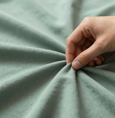 A detailed close-up of a hand feeling a soft, sage mist green fabric. The lighting is natural and diffuse, highlighting the premium quality of the material. Artistic and calm.