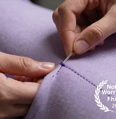 A close-up detail shot of professional hand-stitching on a soft lavender textile, highlighting the artisanal quality of the brand.