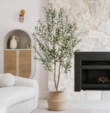 Tall artificial olive tree in a woven basket next to a modern fireplace and white stone wall.