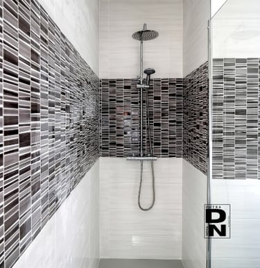 Instalación de ducha empotrada con mampara de cristal y revestimiento de azulejos grises y blancos en baño moderno. Proyecto 