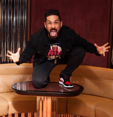 Drummer Lucas Dias crouching on a coffee table, making a funny pose and pulling a silly face.