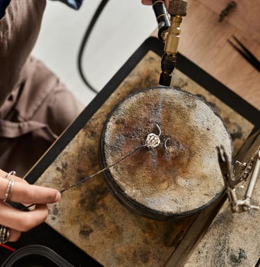 Joyero usando un soplete para soldar un anillo de plata sobre un bloque de soldadura en un taller