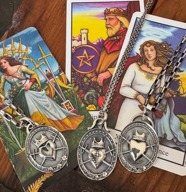 Three silver crowned heart pendants on chains resting on tarot cards with spiritual imagery.