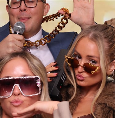 Friends posing with fun photo booth props like a gold chain, retro phone, and oversized sunglasses.
