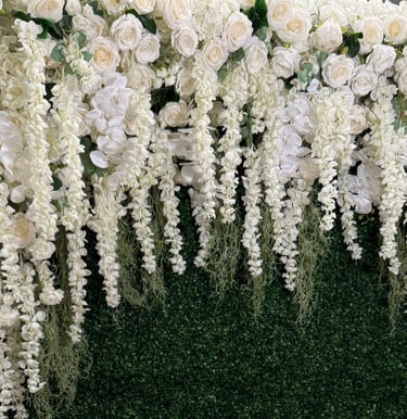Elegant white floral wall featuring roses and hanging wisteria against a lush green boxwood hedge backdrop.