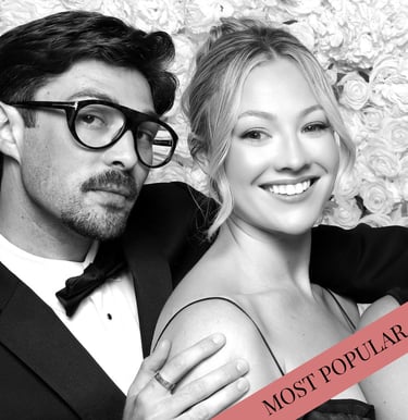Elegant couple posing for a black and white wedding photo booth portrait with a flower wall backdrop.