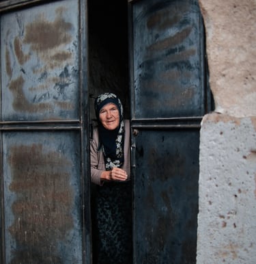 Elderly woman in a headscarf peeking through a weathered metal door in Cappadocia, Turkey