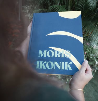 Person holding Moris Ikonik book against tropical background in Mauritius