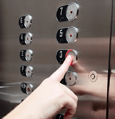 a hand pressing the 3rd floor button on a control operating panel inside an elevator