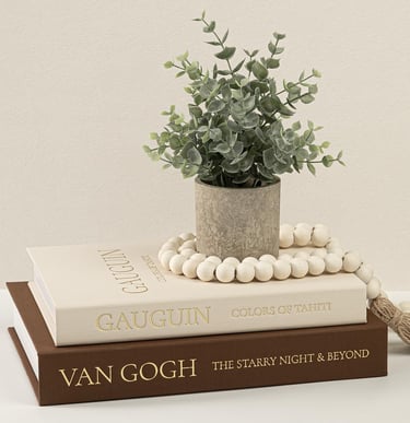 Artificial eucalyptus plant in a stone pot on stacked Van Gogh and Gauguin art books.