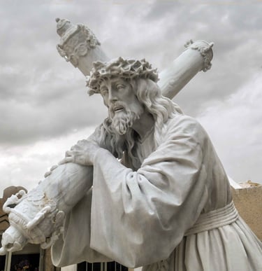 White marble statue of Jesus Christ carrying the cross with a crown of thorns against a cloudy sky.