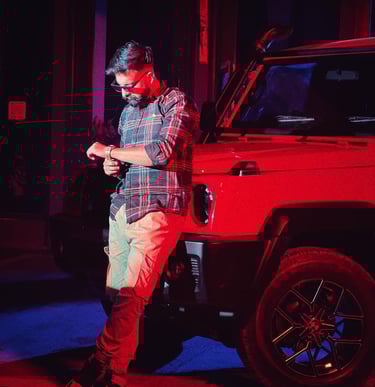 a man in a plaid shirt and jeans standing in front of a red car