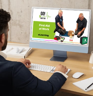 a man at a computer desk looking the computer screen showing a first aid course