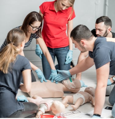 a group of people around a first aid training manikin learning CPR with an instructor