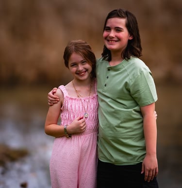 Two happy children, a girl in a pink jumpsuit and a boy in a green shirt, smile at Dow Lake Athens 