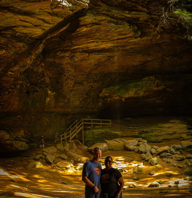 A couple and their dog posing in front of a massive rock cave and waterfall at Hocking Hills State Park.