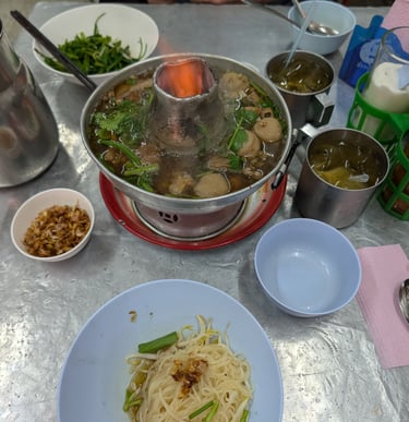 Authentic Thai beef hot pot with meatballs and noodles served on a street food table with a live flame.