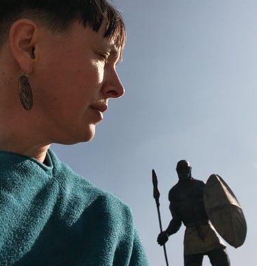 A profile view of a woman in a blue sweater near a historical warrior statue with a shield and spear.