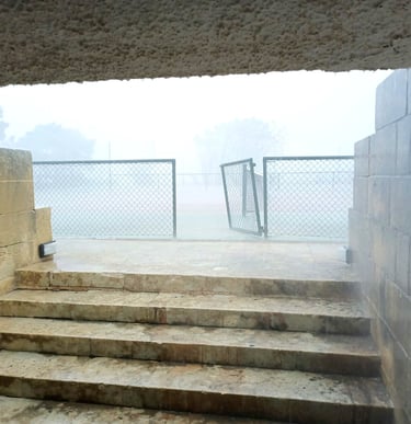 Rainy stone steps leading to a foggy outdoor sports court with a chain link fence gate.